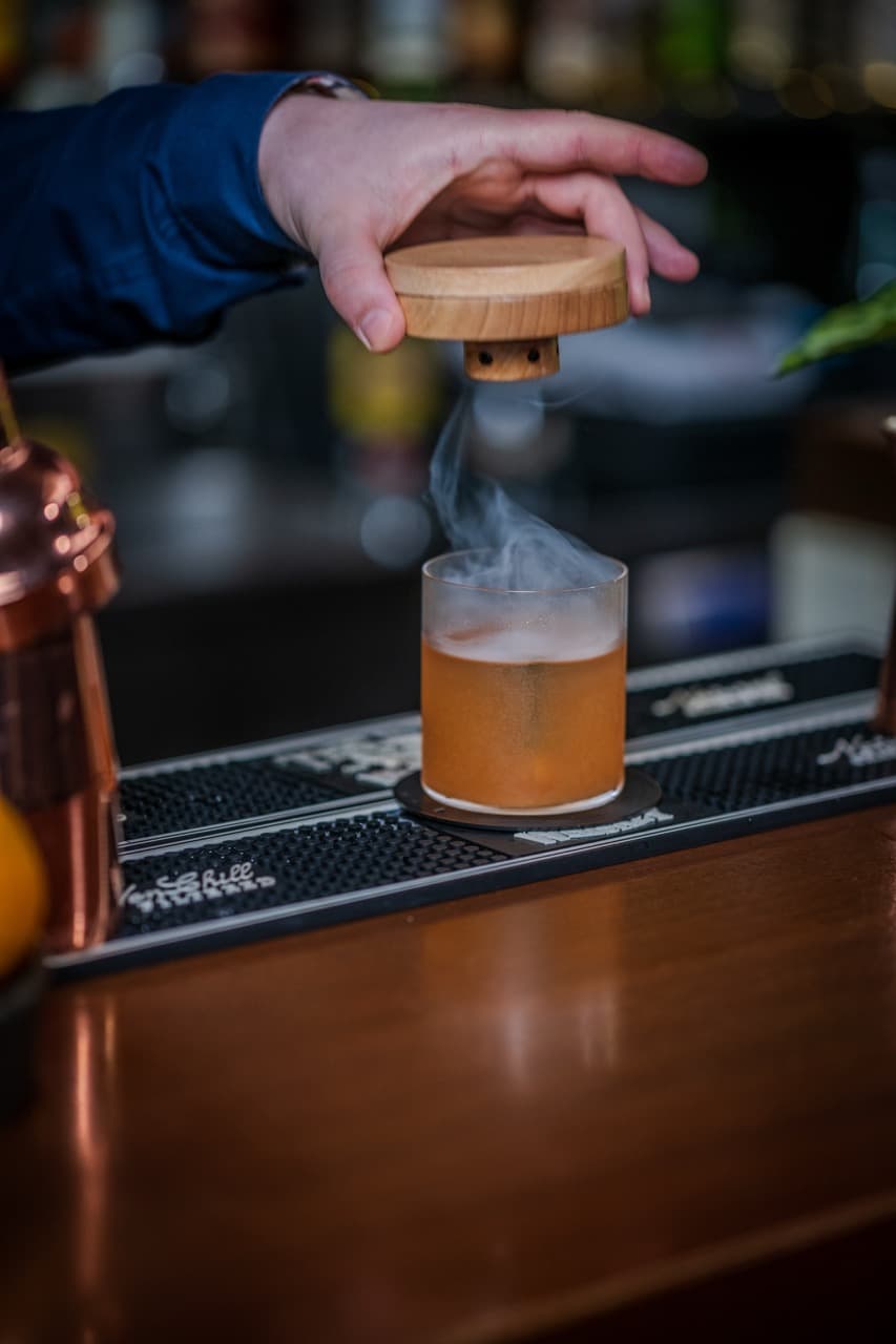 Close-up of a bartender smoking an old fashioned, epitomizing the vibrant yet sophisticated setting of a luxury Maltese bar