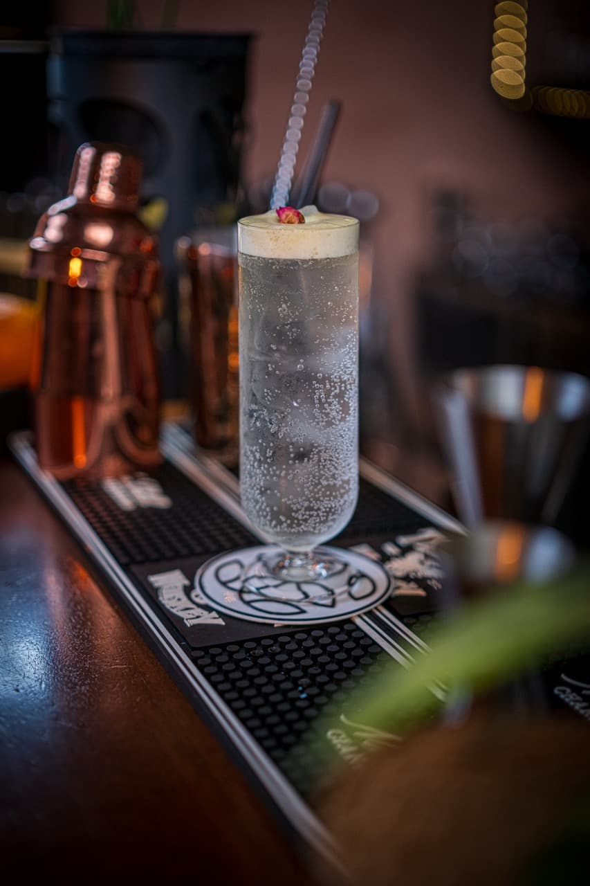 Tall glass cocktail with foam and a fresh herbal sprig, set against the warm glow of premium spirits in a chic Paceville bar