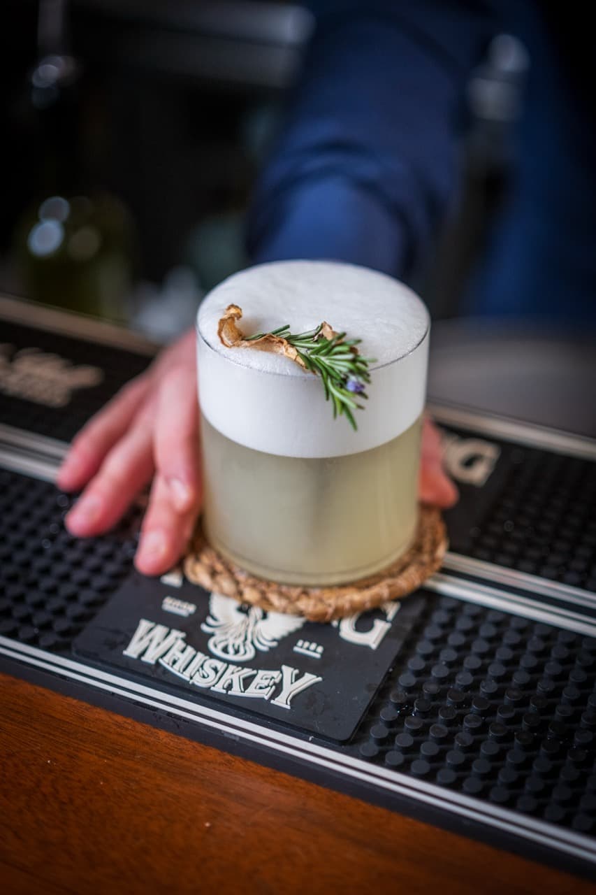Close-up of a bartender carefully placing a mint garnish on a craft cocktail, capturing the refined mixology culture of Malta