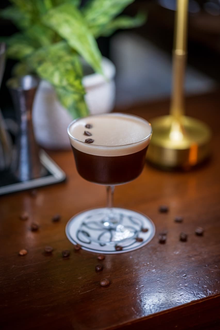 Golden-hued cocktail on a sleek wooden counter, framed by luxury bar tools and citrus accents in a stylish Paceville venue
