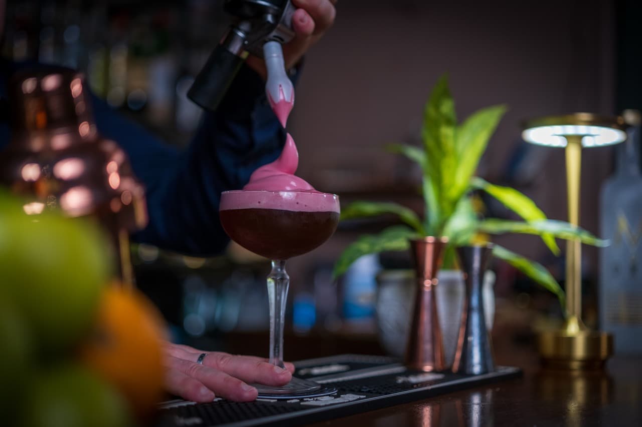Bartender’s hand expertly topping a creamy cocktail, reflecting the intimate and modern ambiance of a high-end Maltese bar